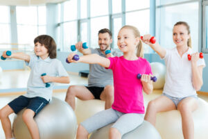 Four smiling gym goers with hand weights atop balance balls